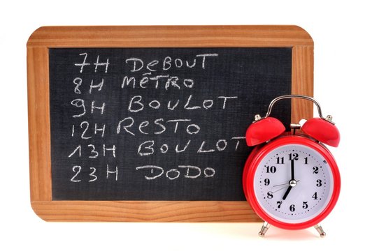 R&eacute;veil matin pos&eacute; &agrave; c&ocirc;t&eacute; d'une ardoise sur laquelle est r&eacute;sum&eacute; l'emploi du temps d'une journ&eacute;e 