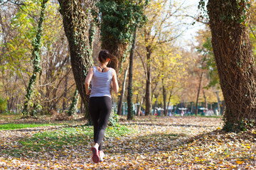 behind view of young woman jogger in autumn woods 