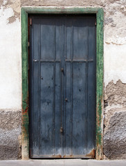 old black doouble doors on a house wall with crumbling plaster walls and green painted frame