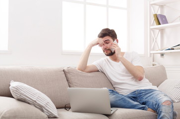 Serious young man at home with laptop and mobile