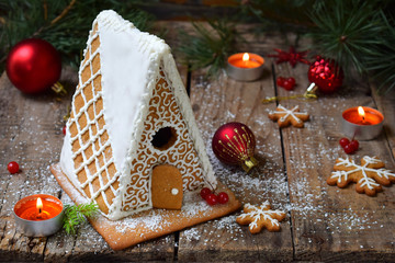 Homemade gingerbread house with pine branches, cones and biscuits on dark background. European Christmas traditions. Xmas holiday sweets.