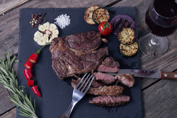 Grilled beef striploin steak from black angus and vegetables on stone plate. Salt and papper. Glass of vine. Top view.