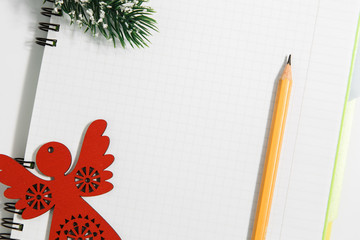 Notebook and yellow pencil with wooden red angel, conifer branch on a white background