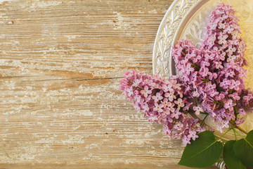 Beautiful lilac flowers lying on a silver saucer against the background of an old wooden plank with a texture paint