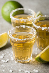 Macro focus photo of shots of golden Mexican tequila with lime and salt on wooden background. Alcoholic drink concept.