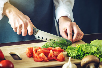The chef in black apron cuts vegetables. Concept of eco-friendly products for cooking