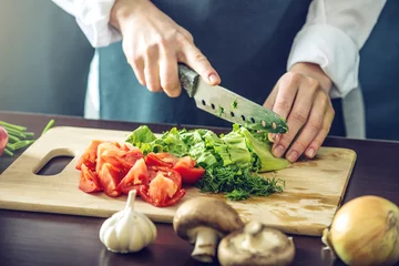 Photo sur Aluminium Cuisinier Le chef en tablier noir coupe les légumes. Concept de produits écologiques pour la cuisson
