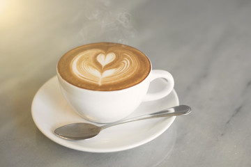 closeup hot coffee latte art cup with smoke on table.