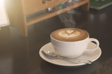 closeup hot coffee latte art cup with smoke on table.