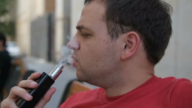 Close up portrait of a man exhaling vapor using electronic cigarette in slow motion