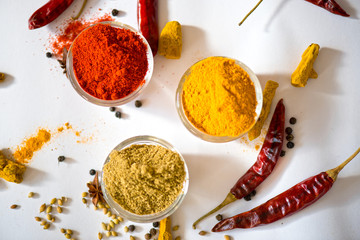 A close-up of three glass bowls filled with chili powder, turmeric powder, and coriander powder,...