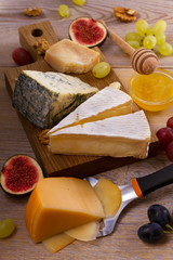 Cheese plate. Various types of cheese with grapes, honey, figs and nuts on rustic wooden table, vertical