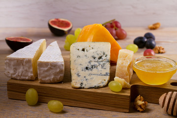 Cheese plate. Various types of cheese with grapes, honey, figs and nuts on rustic wooden table, horizontal