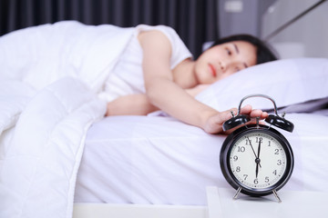 woman sleeping on bed and rise hand to turn off alarm clock in bedroom