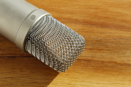 A condenser microphone on a wooden table. This image can be used to represent recording or pod casting. 