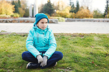 Beautiful teenage girl dressed in a warm jacket and hat sitting on the grass in the autumn.