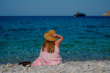 Young girl in a straw hat on the beach enjoying the beautiful view. View from the back.