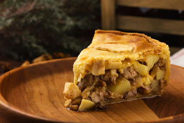 Piece of chicken meat pie with potatoes, apples and chanterelles on a wooden plate