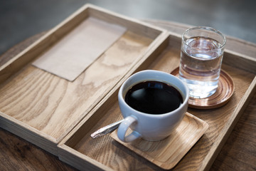 Closeup image of a cup of hot coffee and a glass of water in vintage wooden tray on the table in cafe