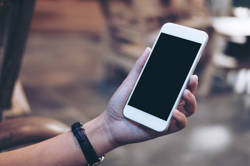 Mockup image of a woman's hand holding white mobile phone with blank black screen , concrete floor background