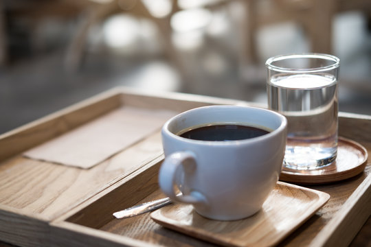 Closeup image of a cup of hot coffee and a glass of water in vintage wooden tray on the table in cafe