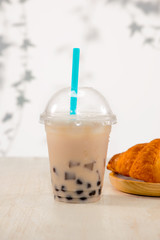 Light brown creamy bubble tea and black tapioca pearls  in plastic cups on table.