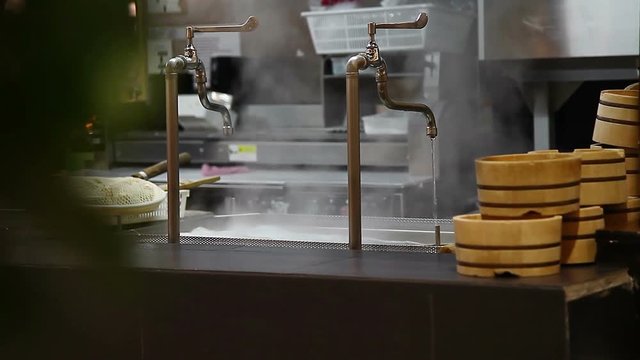 The faucet is turned on for the water is boiling in big pot. It was equipment for make Japanes noodle(Udon) Within a Japanese restaurant and have a bowl wood Place the lined ready for Serve.