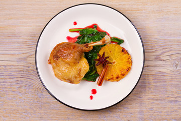 Duck leg with spinach and orange in sweet and sour berry sauce, white plate on rustic wooden table