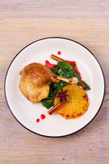Duck leg with spinach and orange in sweet and sour berry sauce, white plate on rustic wooden table