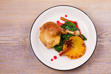 Duck leg with spinach and orange in sweet and sour berry sauce, white plate on rustic wooden table