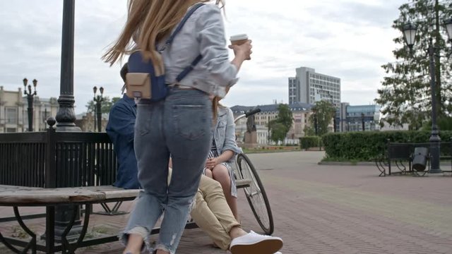 Zoom In Of Couple Sitting On Bench And Talking While Their Friends Walking To Them With Coffee, Men Greeting Each Other With Bumping Fists, Young People Talking And Smiling