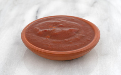 A small bowl of adobo sauce atop a gray marble counter top.