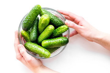 Hands take fresh cucumbers in bowl. White background top view copyspace
