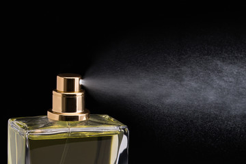 Close Up Studio Shot Of Cosmetic Perfume In Glass with The Nozzle Spraying And Splashing On Black...