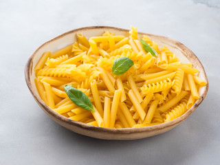 Italian raw short pasta in a dish with basil leaves on gray background