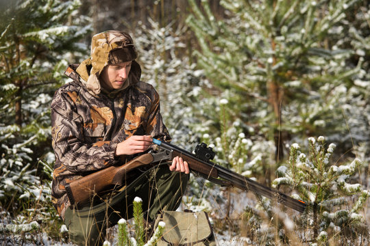 Hunter with a backpack and a hunting gun in the winter forest. Man is charging a hunting rifle. Winter snow-covered forest.