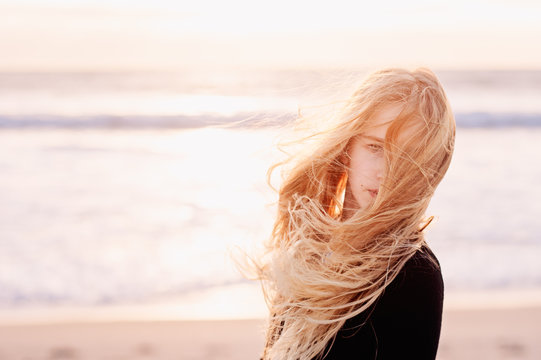 Pre-teenage girl with very windswept long blonde hair at the beach in winter