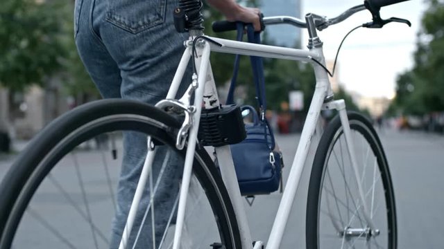 Tilt down closeup shot of woman walking with bicycle along paved street in the city