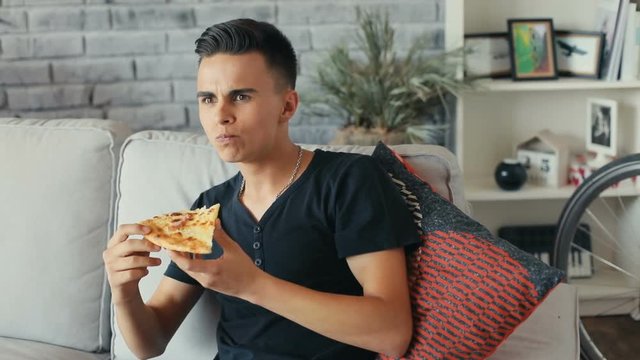 handsome young man sitting on the sofa at home eating pizza smiling food tasty cheese cute dinner eating fast food hunger man young delicious Shot on RED Epic Camera. Slow motion