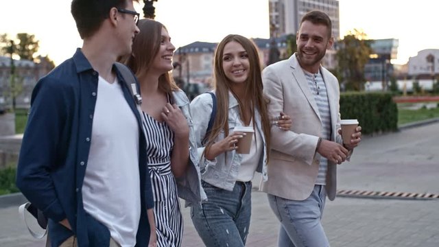 Tilt up of young men and women on double date outdoors: couples holding coffee cups, talking and laughing during walk