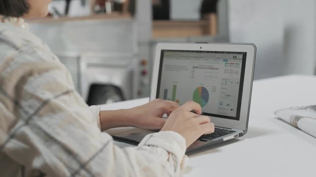 Young professional business woman uses laptop at co-working startup hub space office, creates graphs and charts for financial data and key performance indicators for business access ideas