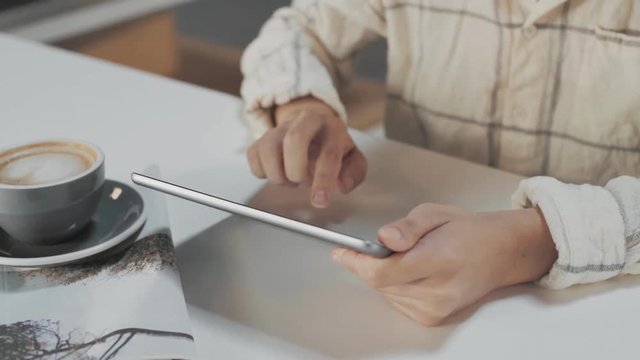 Top side view on hands typing message or mail in portable touch screen tablet at moning, next to newspaper and coffee cup with flat white, isolated on table