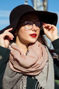 Fashion portrait of pretty young model walking at the city. Woman wearing fashionable hat, scarf and glasses