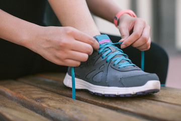 Young woman tying the shoelaces of her fitness shoes on a bench