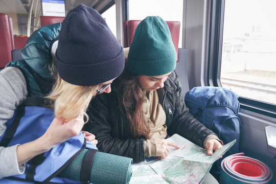 Two girlfriends traveler with backpacks and inventory go in the train and watch the further route on the map