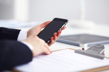 Businesswoman using her phone in office sitting on desk, selective focus