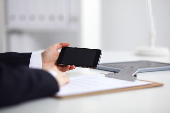 Businesswoman using her phone in office sitting on desk, selective focus