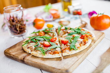 hot fresh homemade traditional italian pizza with cheese, tomatoes and rocked salad on wooden cooking table. wallpaper for pizzeria and food concept