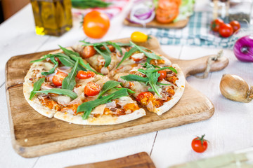 hot fresh homemade traditional italian pizza with cheese, tomatoes and rocked salad on wooden cooking table. wallpaper for pizzeria and food concept