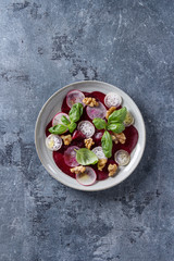 Vegan beetroot carpaccio salad with radish, basil, olive oil and walnuts in ceramic plate over blue texture background. Top view, space. Healthy eating